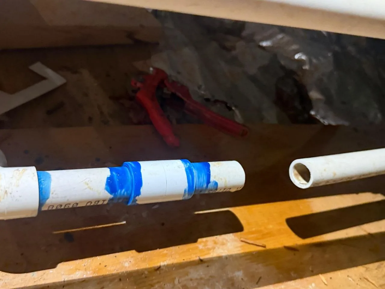 Cut PVC condensate drain line with a red ratcheting pipe cutter resting in the drain pan behind it
