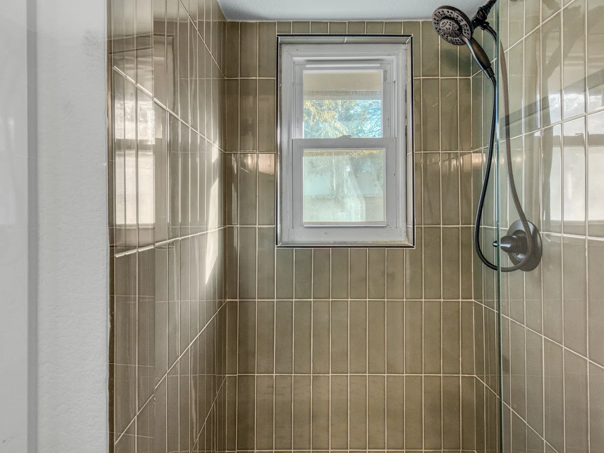 Completed walk-in shower with olive green stack bond tile and a glass enclosure